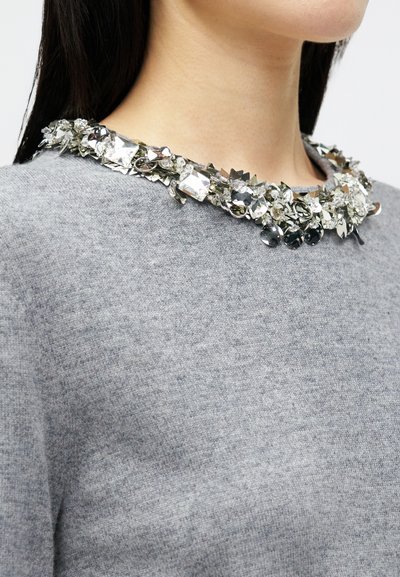 Γκρι πουλόβερ με διακοσμητικό γιακά από ασημί και διάφανα κοσμήματα, με διάφορα σχήματα και υφή πλέξιμο.