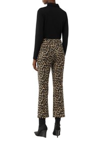 Black long-sleeve top and leopard print flared trousers, featuring a beige background with black spots, paired with black heeled ankle boots.