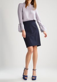 Ljuslila blus med utsvängda ärmar, kombinerad med en marinblå pennkjol och blå högklackade sandaler med vristremmar.