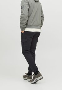 Grå zip-up jacka med vit ribbad fåll, kombinerad med svarta cargo-byxor med sidofickor. Grå sneakers med svarta accenter.