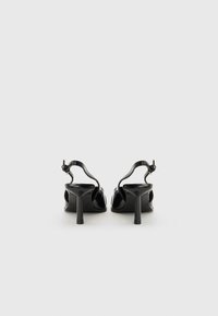 Svarta lackläder högklackade skor med slingback-design, som har ett tunt band och en cylindrisk klack. Slät, glänsande yta.