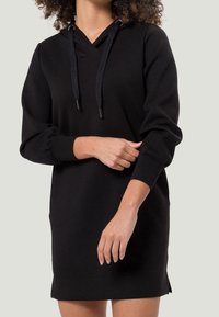 Robe sweat à capuche noire avec encolure en V et cordon tressé, dotée de manches longues avec poignets élastiques et de fentes latérales à l'ourlet. Matière douce.