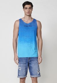 Zilā gradienta topiņš ar apaļu kakla izgriezumu, ar smalku faktūru un melnā krāsā izdrukātu "Kairoshi Brand". Apvienots ar nolietotiem džinsu šortiem.