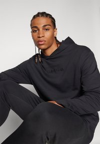 Čierna mikina s kapucňou od Calvin Klein s uvoľneným strihom, ktorá má vyšívané logo na hrudi, mäkkú textúru a veľkú kapucňu.