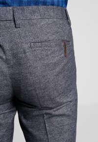 Men's gray textured trousers featuring a single back pocket with a brown label, crafted from a woven fabric with subtle patterns.