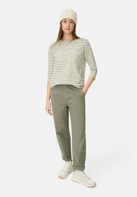 Stribet beige langærmet top, olivengrønne bukser, cremet hue og lyse sneakers. Løs pasform med oprullede manchetter og sidelommer.