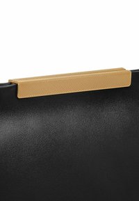 Sac à main en cuir noir avec un accent en métal doré texturé sur le dessus. Présente une finition lisse et une forme structurée.
