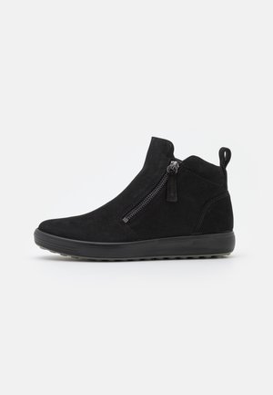 Bota de ante negra hasta el tobillo con cremallera lateral, lengüeta en el talón y suela gruesa de goma con dibujo para agarre.