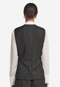 Grå herringbone-väst med en figursydd design, som har en slät vit skjorta under. Baksidan visar skräddarsydda sömmar och inga synliga fickor.