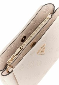 Sac à main rose clair en matériau texturé avec une fermeture éclair dorée et des accessoires en or. Présente un motif de logo en relief et une forme structurée.