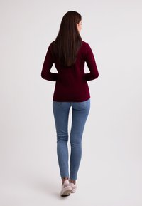 Bordowy długi rękaw, dopasowane jasnoniebieskie jeansy i białe trampki z różowymi akcentami. Gładki materiał i casualowy design.
