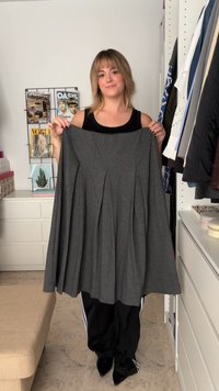 Jupe plissée grise en tissu doux, dotée d'une ceinture. Le mannequin la tient devant un fond clair avec des magazines en arrière-plan.