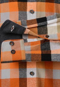 Flannel skjorte med sort, orange, grå og hvid ternet mønster. Indeholder sorte knapper og et broderet logo på manchetten.