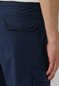 Marineblaue Cargo-Shorts mit aufgenähten Taschen, glatter Textur und verstärkten Nähten an den Kanten. Einfaches Design mit utilitaristischem Stil.