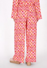 Multicolore wijdvallende broek in een hartpatroon met roze, oranje en gele tinten, gemaakt van lichte stof.