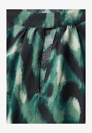 Geplooide stofdetail met een groen en zwart abstract patroon, voorzien van een kleine sleutelgatopening, gemaakt van zacht, textuurvol materiaal.