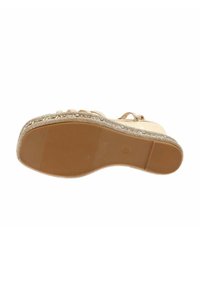 Sandal beige con suola texturizzata, presenta accenti metallici decorativi lungo il bordo e una superficie superiore liscia con design a strappo.