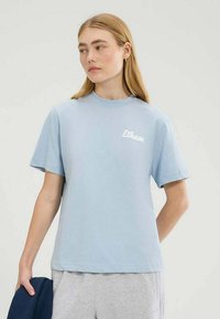 Lichtblauw katoenen T-shirt met een ronde hals en korte mouwen, voorzien van een wit logo op de linkerkant van de borst. Eenvoudig en ongecompliceerd ontwerp.