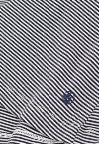 Tessuto a righe blu navy e bianche con una texture morbida. Presenta un piccolo logo ricamato nell'angolo in basso a sinistra e un orlo cucito.