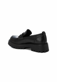 Mocasines de cuero negro con una suela de goma baja y gruesa. Presentan un acabado suave y un detalle decorativo en la parte superior.