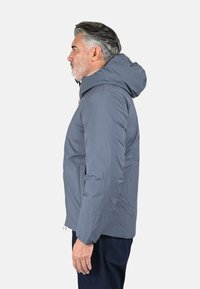 Veste matelassée grise avec capuche, au design épuré, texture douce et fermeture éclair visible, portée sur un haut clair et un jean.