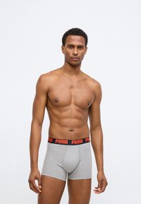 Sivé boxerky vyrobené z bavlny s čiernym a červeným pásom so znakom Puma. Strih je priliehavý a dĺžka je do polovice stehna.