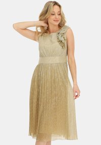 Złota sukienka do kolan z jednym ramieniem i falbaniastym wykończeniem. Wykonana z teksturowanej, błyszczącej tkaniny, z dopasowanym topem i plisowaną spódnicą.