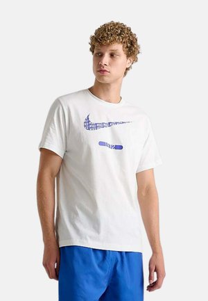 Giovane uomo con capelli ricci che indossa una maglietta bianca Nike con logo blu e pantaloncini blu, guarda leggermente verso sinistra.
