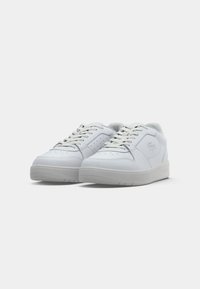 White leather sneakers with a smooth texture, round toe, and perforated detailing. Lace-up design and a light rubber sole.