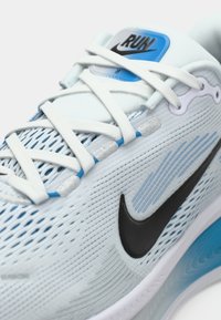 Chaussure de course bleu clair et blanche avec des lacets blancs, un logo Nike noir et une étiquette bleue portant le mot "RUN" sur la languette.