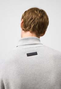 Szary sweter z prążkowanego dzianiny z wysokim kołnierzem i czarną metką z tyłu, z delikatną pionową fakturą i dopasowanym krojem.