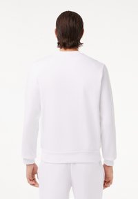 Weißes Crewneck-Sweatshirt aus weichem Material mit langen Ärmeln und gerippten Bündchen. Glatte Textur mit minimalistischer Gestaltung.