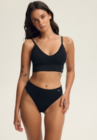 Czarny, gładki bralet z cienkimi ramiączkami i dekoltem w kształcie litery V, w połączeniu z czarnymi majtkami bikini o wysokim stanem z metką z logo.