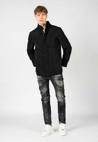 Giacca casual nera con tasche sul petto con zip, abbinata a jeans grigi logori e sneakers bianche. Tessuto morbido, design strutturato.