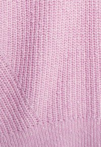 Zbliżenie na miękką, teksturowaną różową dzianinę z pionowym ryżowym splotem i ukośnymi wzorami ściegów.