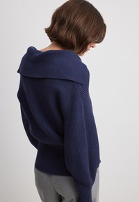 Navy blue knit sweater with a wide, folded collar, textured finish, and loose fit, featuring drop shoulders and a gently cinched waist.