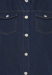 Chemise en denim bleu foncé avec boutons métalliques sur le devant et deux poches poitrine à boutons avec coutures apparentes.