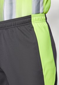 Sport-Shorts in Dunkelgrau mit leuchtend grünen seitlichen Einsätzen. Leichtes Material mit strukturiertem Muster. Elastischer Bund für zusätzlichen Komfort.