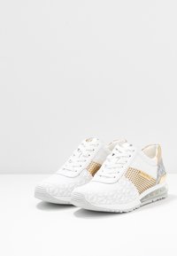 Zapatillas blancas con paneles de malla y texturizados, acentos dorados y una suela translúcida con un diseño estampado. Estilo con cordones.