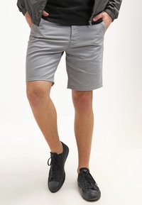 Grijze shorts van lichtgewicht stof, met een slim fit, zijzakken en een platte voorkant, gedragen met zwarte sneakers.