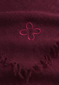 Sciarpa bordeaux con una texture morbida, caratterizzata da un dettaglio di un fiore ricamato rosa e bordi frangiati.