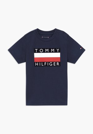 Marineblauwe katoenen T-shirt met een groot wit, rood en zwart grafisch ontwerp met de tekst "TOMMY HILFIGER" in blokletters. Korte mouwen, ronde hals.