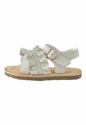 Biela detská sandála s béžovou podrážkou, nariaseným predným remienkom a prackou v tvare srdca zo zlata na remienku okolo členka.