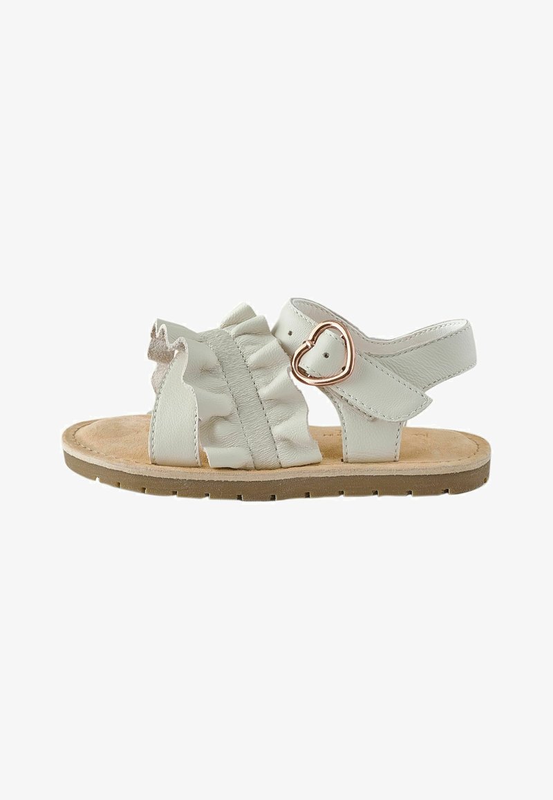 Sandale blanche pour tout-petit avec semelle beige, bride avant à volants et boucle en forme de cœur doré sur la bride de cheville.