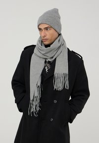 Berretto grigio a maglia e sciarpa abbinata con frange, abbinati a un cappotto nero doppiopetto. Trama morbida, design semplice e colori neutri.