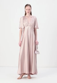 Lungo abito svolazzante color blush in satin con maniche corte a farfalla e scollatura profonda a V. Accompagnato da una piccola borsa morbida.