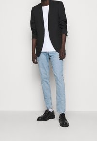 Blazer negro, camiseta blanca, jeans azul claro y zapatos negros. El blazer tiene dos botones y un bolsillo en el pecho. Los jeans tienen un corte recto.