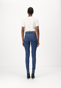 Tummansiniset korkeat farkut, joissa on viisi taskua, nahkapatentti takana, yhdistettynä vaaleanbeigeen t-paitaan ja mustiin korkokenkiin.