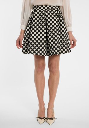 Vrouw met een zwarte rok met grote witte stippen, een crèmekleurige blouse en crèmekleurige puntige hakken met zwarte strikjes.