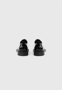 Chaussures en cuir verni noir avec un bout arrondi, un talon plat et une petite languette à l'arrière. Texture lisse avec un minimum de surpiqûres.